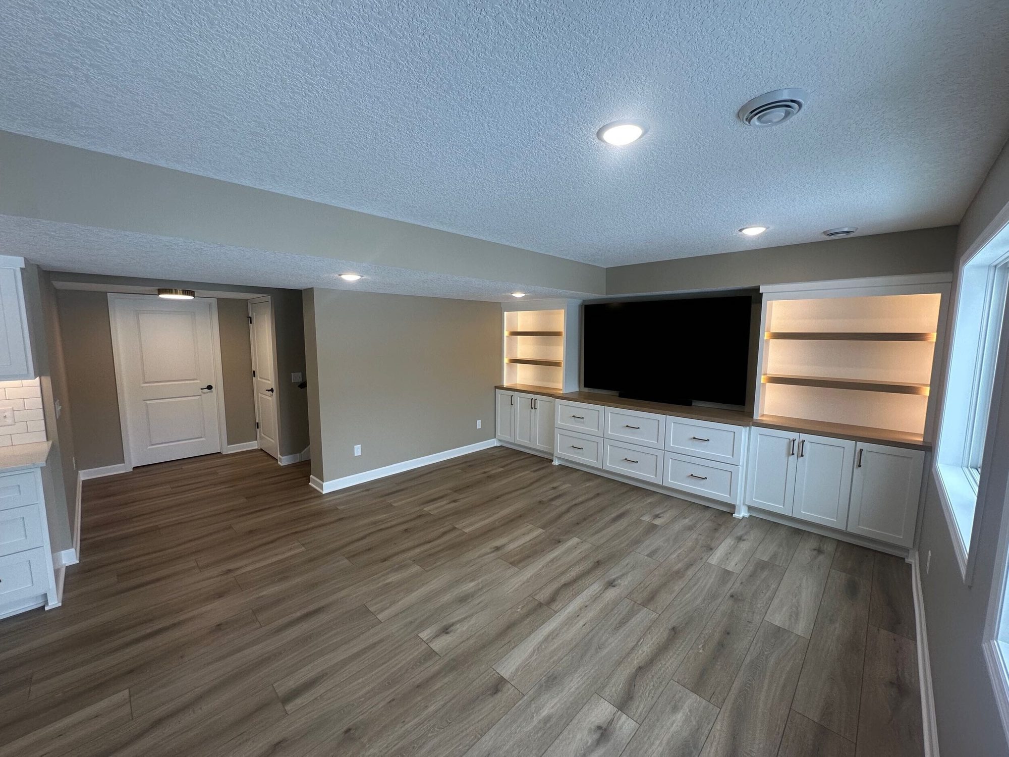 A finished basement in Chanhassen, MN with a wall-mounted TV, built-in shelving, and wood-look flooring by BN Builders.