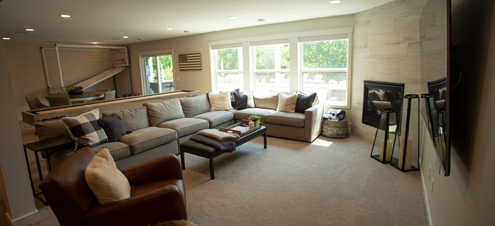 A finished basement living space in Chanhassen, MN with a sectional sofa, leather seating, carpeted floor, and a wall of windows by BN Builders.