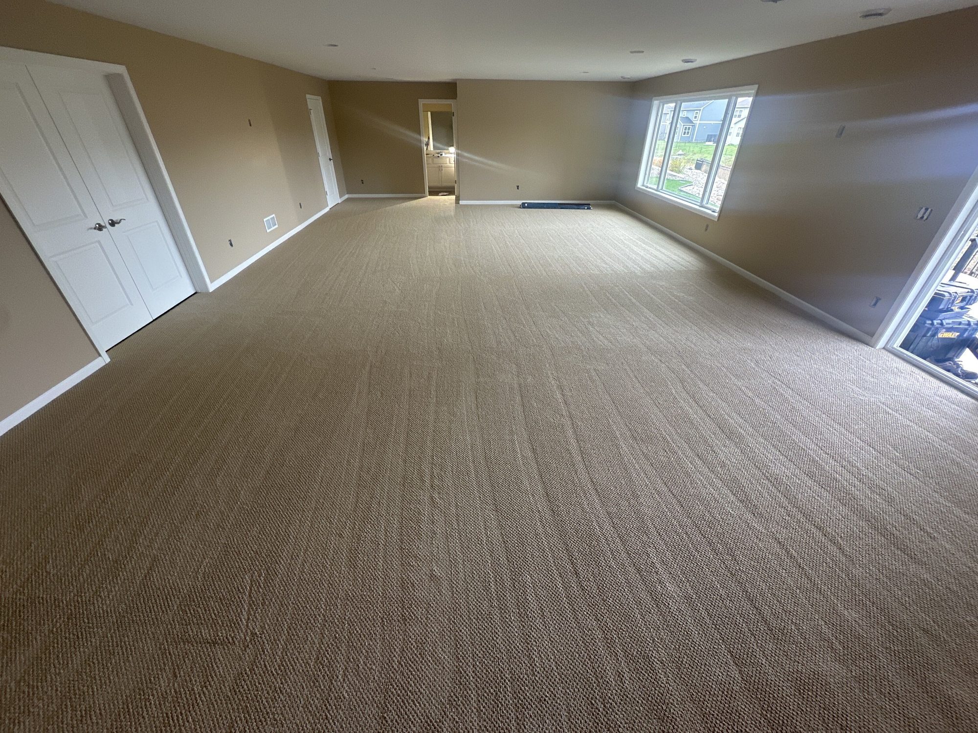 A large open finished basement room in Newport, MN with fresh neutral carpet, painted walls, and egress windows by BN Builders.