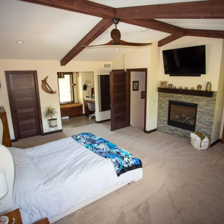 Spacious master bedroom featuring exposed wooden beams, a stone fireplace, and rustic decor, creating a warm and inviting atmosphere.
