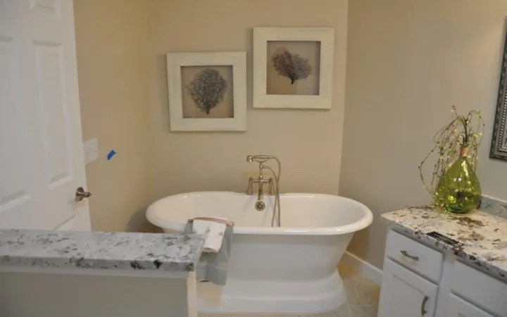 A freestanding bathtub in a bathroom, with art wall displays, marble countertops and white cabinets