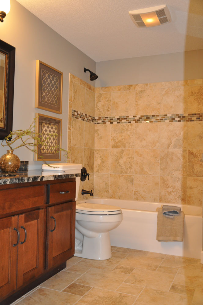 A modern bathroom featuring a dark wood vanity with granite countertop, a tiled shower with decorative mosaic border, and framed artwork on the walls.